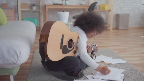 Afroamerikanerin mit Afrofrisur komponiert ein Lied und spielt auf dem Boden sitzend Gitarre — Stockvideo