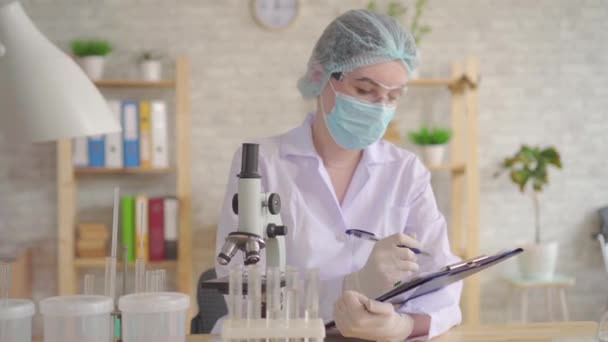 Close-up de uma assistente de laboratório feminina realiza e registra o estudo usando um microscópio — Vídeo de Stock