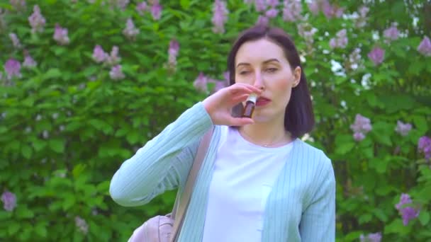 Retrato de una mujer joven usando aerosol nasal alérgico en el fondo de las plantas con flores en el Parque — Vídeo de stock