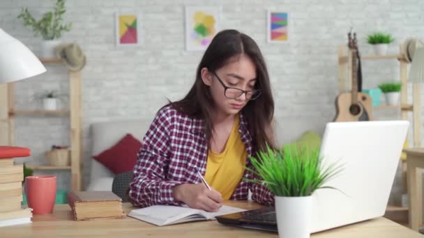 Bela menina asiática na sala de estar em casa, sentado à mesa com um laptop e estudando — Vídeo de Stock