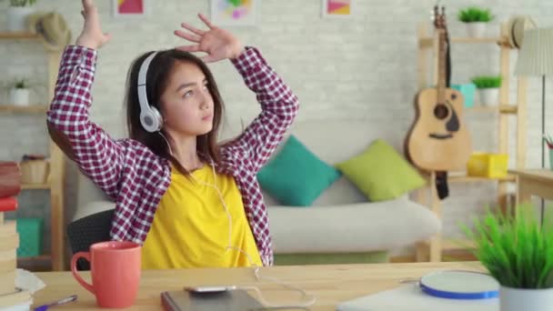 Bela menina asiática com cabelos longos na sala de estar de uma casa moderna com fones de ouvido ouvir música e relaxante — Vídeo de Stock