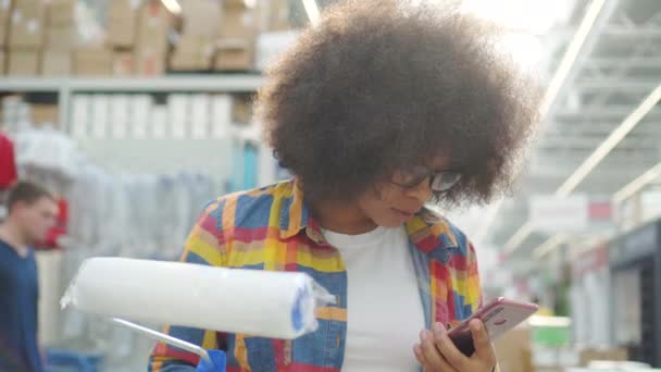 Portrait femme africaine avec une coiffure afro avec le téléphone en main dans le magasin dans le département tout pour la réparation — Video