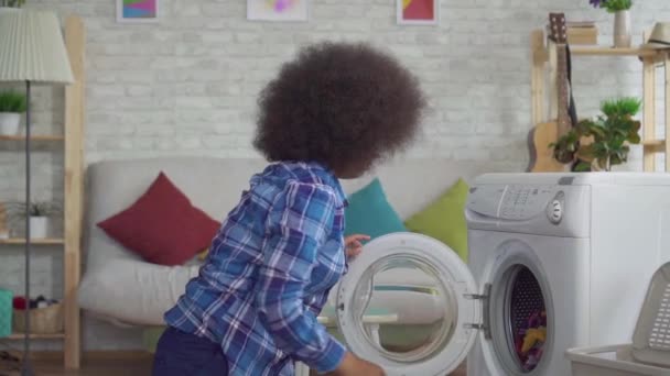Cansada mujer africana con un peinado afro pone ropa sucia en la lavadora lenta mo — Vídeo de stock