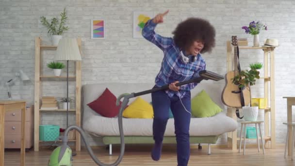 Щаслива африканська жінка з афро зачіскою танцює з мопедом від пилососа у вітальні повільно мо — стокове відео