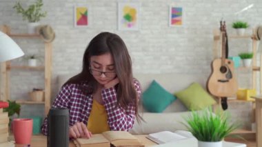 oturma odasında uzun saçlı gözlük güzel Asyalı kız modern bir kitap okuma ve ses asistanı sahiptir