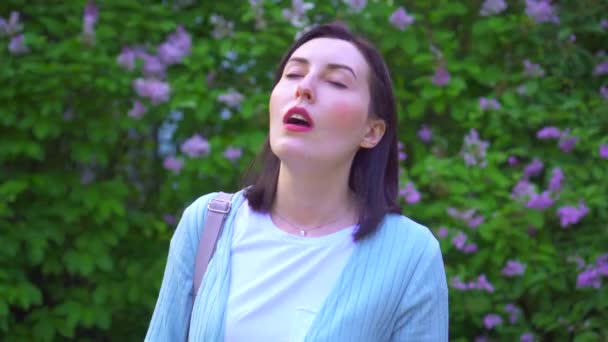Retrato de uma jovem mulher tira a máscara médica e respira profundamente no ar contra o fundo das flores — Vídeo de Stock