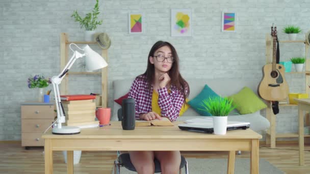 Egy gyönyörű ázsiai lány szemüveg hosszú haja a nappaliban egy modern ház olvas egy könyvet, és használja a hangasszisztens előkészítése vizsgák — Stock videók