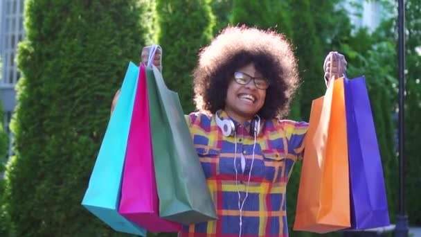 Portrait femme africaine gaie avec une coiffure afro avec des paquets après les achats en regardant la caméra ralenti mo — Video