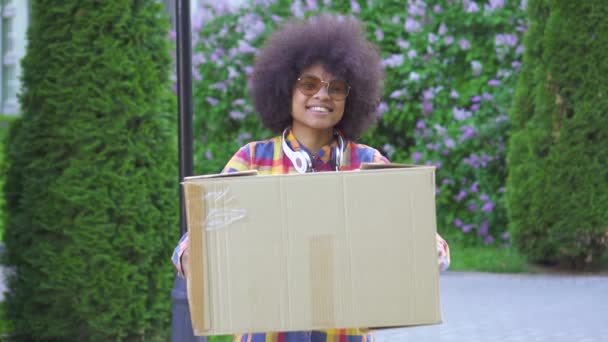 Весёлая африканская американка с афро-прической с коробкой, смотрящая на камеру медленно — стоковое видео