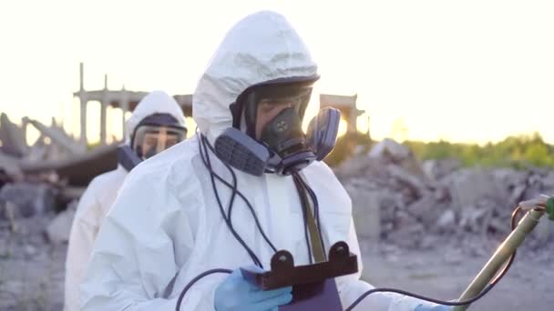 Porträt zweier Wissenschaftler in weißen Overalls und Schutzmasken, die bei Sonnenuntergang im zerstörten Atomkraftwerk Strahlungsmessungen durchführen — Stockvideo