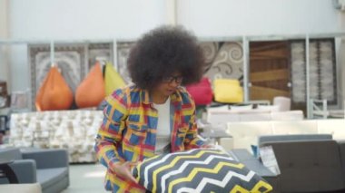 afro saç modeli ile afro-amerikalı kadın bir mobilya mağazasında yastık seçer