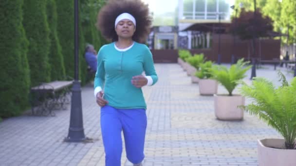 Retrato de una joven atleta positiva mujer afroamericana con un peinado de estilo africano en el fondo del paisaje urbano mirando a la cámara — Vídeos de Stock