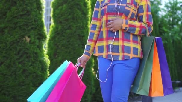 Africká Američanka s afroúčesu, s balíčky po nakupování ve sluchátkách a poslech hudby pomalý mo — Stock video