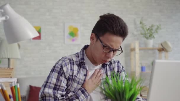 Retrato joven asiático hombre en una camisa asmática disfruta del aerosol de toser sentado en el portátil — Vídeo de stock