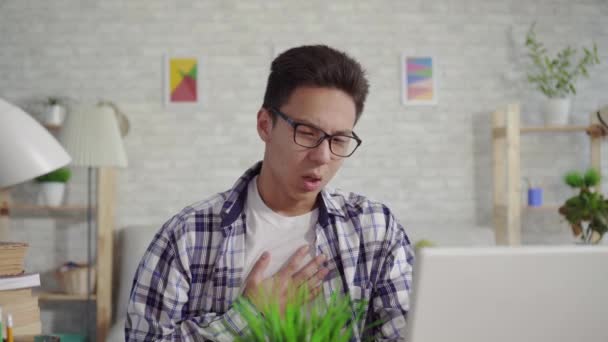 Bir gömlek genç asyalı adam dizüstü bilgisayarda oturan öksürür — Stok video