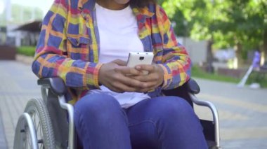 tekerlekli sandalyedeki siyah kadın engelli bir akıllı telefon kullanarak yakın eller