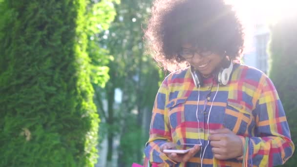 Alışveriş ten sonra paketleri ile bir afro saç modeli ile neşeli afrikalı amerikalı kadın bir akıllı telefon yavaş mo kullanır — Stok video