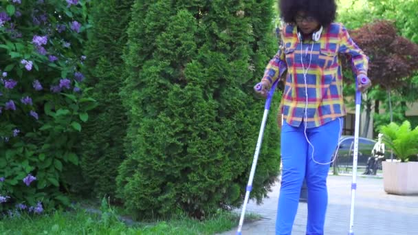 Donna afro americana con un'acconciatura afro con una gamba rotta sulle stampelle slow mo — Video Stock