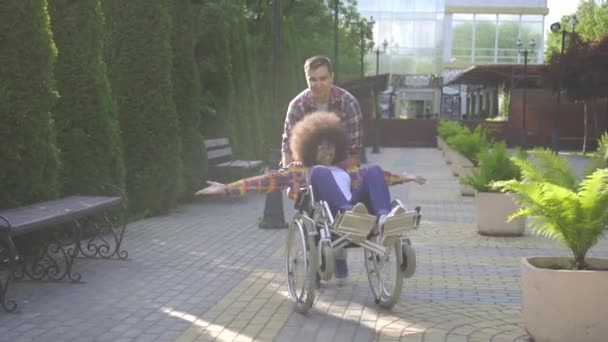 Mujer africana con un peinado afro discapacitado en una silla de ruedas en el parque para un paseo con un amigo divirtiéndose — Vídeos de Stock