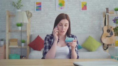 elinde kredi kartı ile sinirli genç kadın modern bir dairede telefonda konuşurken