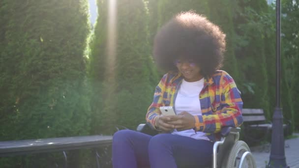 Afrikansk amerikansk kvinna med en afro frisyr funktionshindrade i en rullstol använder en smartphone sunflare — Stockvideo