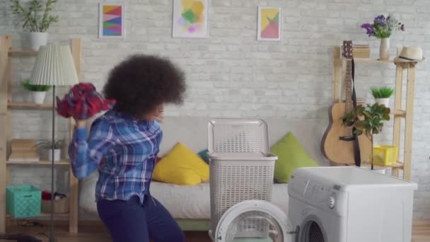 Крупним планом щаслива африканська жінка з афро зачіскою кидає брудний одяг у пральну машину, як м'яч у кошику повільний мо — стокове відео