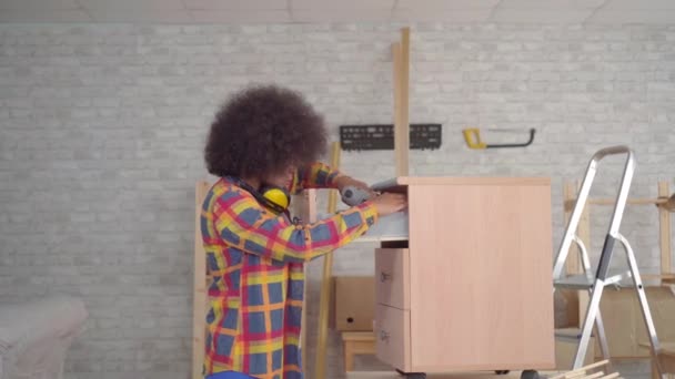 Portræt afrikansk kvinde med en afro frisure ved hjælp af værktøjer, der er involveret i samling af møbler i stuen – Stock-video