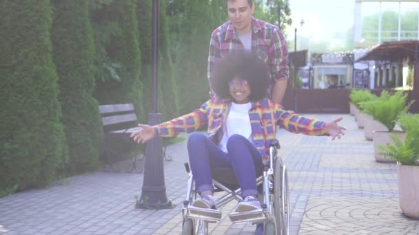 Retrato de uma jovem afro-americana sorrindo positiva com deficiência em uma cadeira de rodas e sua amiga se alegra e levanta as mãos — Vídeo de Stock