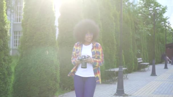 Mujer africana con un fotógrafo de peinado afro con una cámara en el paisaje urbano — Vídeo de stock