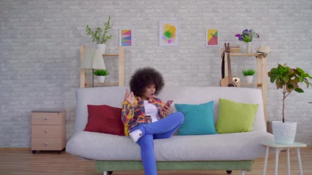 Mujer afroamericana con un peinado afro utiliza un teléfono inteligente tiene buenas noticias y disfruta bailando — Vídeo de stock