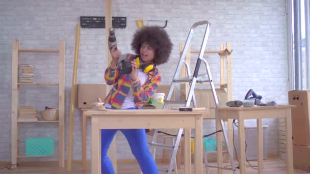 Весело танцює африканська жінка з афро зачіскою працює на дереві в майстерні — стокове відео