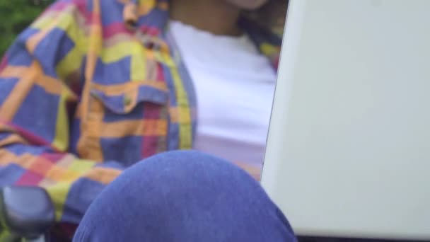 African American vrouw met een Afro kapsel uitgeschakeld in een rolstoel maakt gebruik van een laptop sunflare in Park close-up — Stockvideo