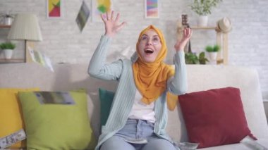 olumlu genç Müslüman kadın evde kanepede oturan düşen banknotlar yakalar