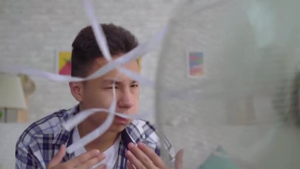 Fiatal ázsiai férfi mentette meg a hőt ülés előtt egy működő ventilátor fogalma hő közelről lassú Mo — Stock videók