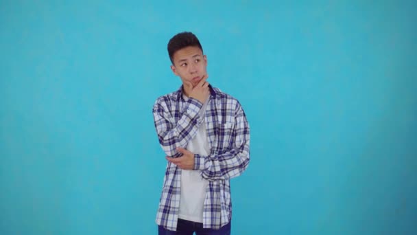 Вдумчивый молодой азиат находит решения на голубом фоне — стоковое видео