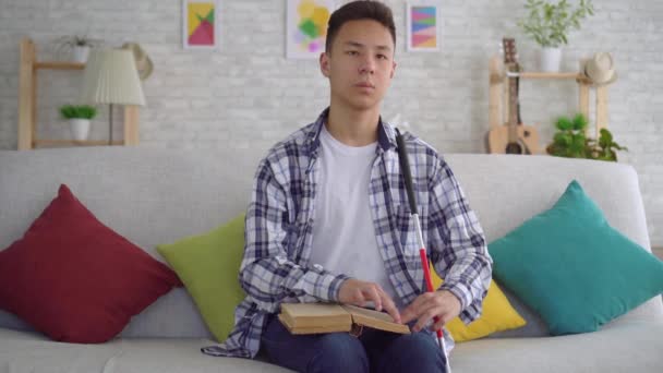 Portré vak ázsiai fiatalember olvasott könyv Braille-szöveg ül a kanapén a nappaliban — Stock videók