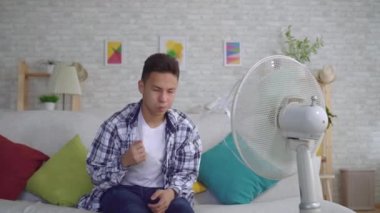 Genç asyalı adam ısı kavramı çalışan bir fan önünde oturan ısı kurtardı