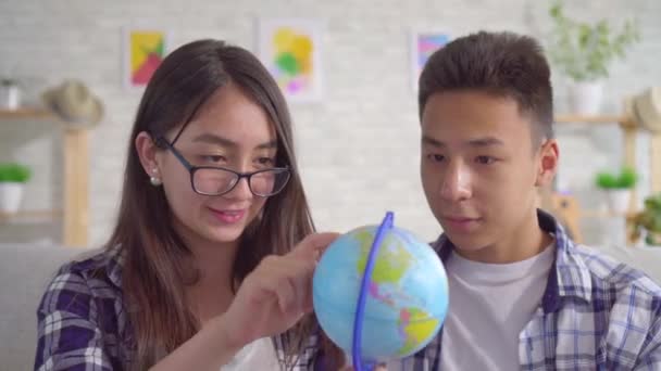 Unga positiva asiatiska paret med en jordglob i sina händer planerar en resa — Stockvideo