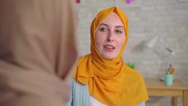 Две красивые глухие молодые мусульманки в хиджабах разговаривают с языком жестов в гостиной рядом с домом — стоковое видео
