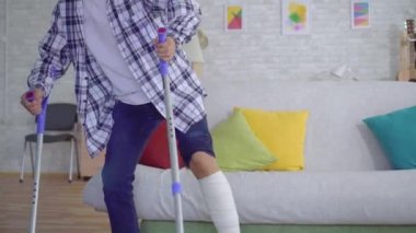 Koltuk değnekleri kanepede oturan bandajkırık bacak ile Yorgun Asyalı genç adam