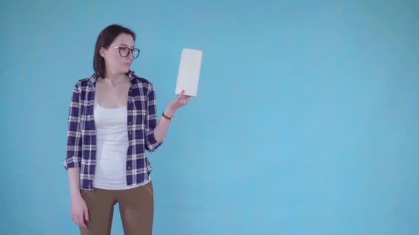 Απογοητευμένος νεαρή γυναίκα στέκεται σε μπλε φόντο και κρατώντας χαρτί πετσετών — Αρχείο Βίντεο