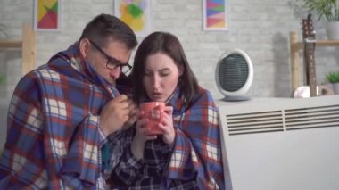 Dondurulmuş genç kadın ve adam oturma odasında bir battaniye ye sarılmış elektrikli ısıtıcılar yakın yanında ısıtılır