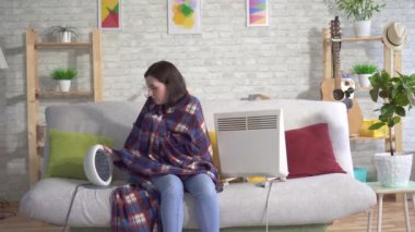 Oturma odasında Dondurulmuş genç kadın ve elektrikli ısıtıcılar yanında güneşlik