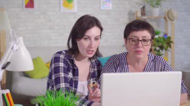 dizüstü bilgisayarbaşında oturan genç kadın orta yaşlı bir kadına işitme cihazının nasıl kullanılacağını anlatıyor