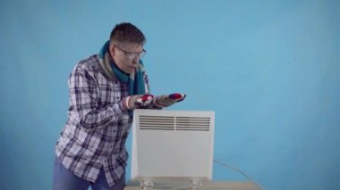 Dondurulmuş adam don ve eldiven ile kaplı mavi bir arka plan üzerinde elektrikli ısıtıcı yanında ısır