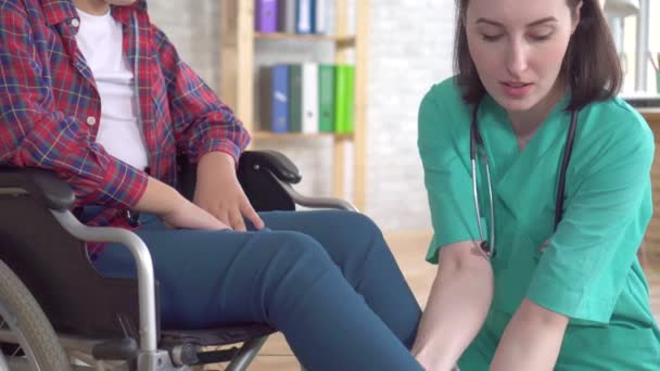 Врач в клинике осматривает ногу девочки-подростка с инвалидностью в инвалидном кресле — стоковое видео