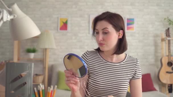 Distressed young hard of hearing woman puts a hearing aid on her ear and looks in the mirror — Stock Video