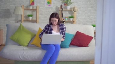 bir laptop üzerinde çalışan kanepede oturan kadın hemoroid ağrı ve rahatsızlık yaşanıyor