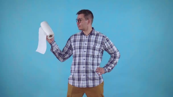 Joven positivo parado sobre un fondo azul y sosteniendo toallas de papel — Vídeos de Stock