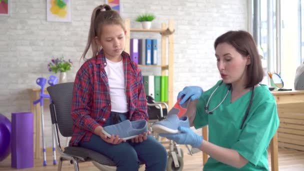 Médico ortopédico diz a uma adolescente sobre palmilhas ortopédicas — Vídeo de Stock